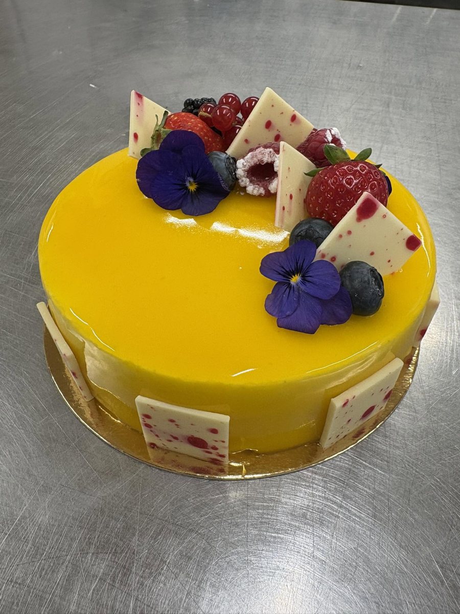 Entremets au glaçage miroir décoré de fruits rouges et de pensées